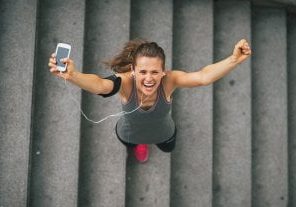 Portrait of happy fitness young woman with cell phone outdoors in the city rejoicing